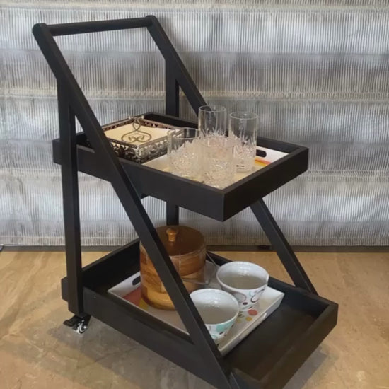 An video of a two tier cocktail serving trolley, with glasses and napkins on top and an Ice cube bucket and bowls in the bottom tier. View from the front angle