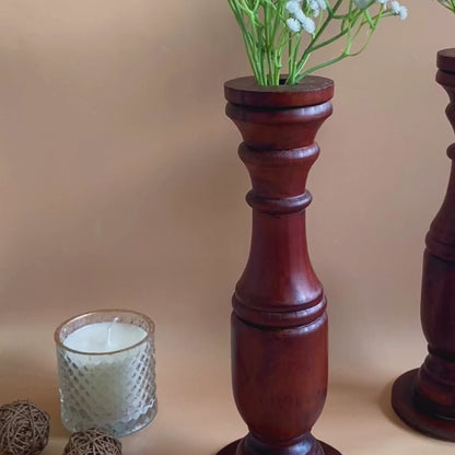 An video of Two wooden hand carved flower vases with white flowers on top and an unlit candle with fur like balls on the side